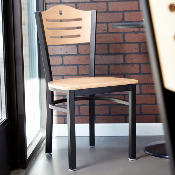 A Lancaster Table & Seating black bistro chair with a natural wood seat and back next to a window.