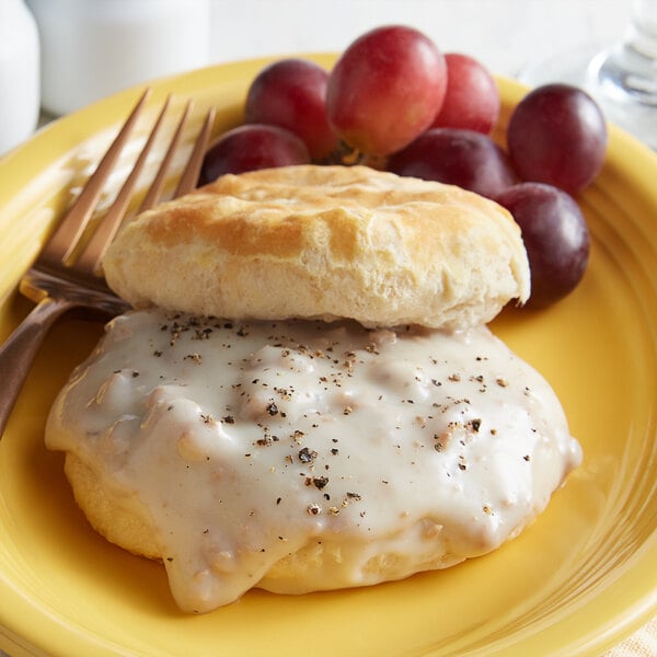 A yellow plate with a biscuit and Vanee Country Style Sausage Gravy with a fork and grapes.