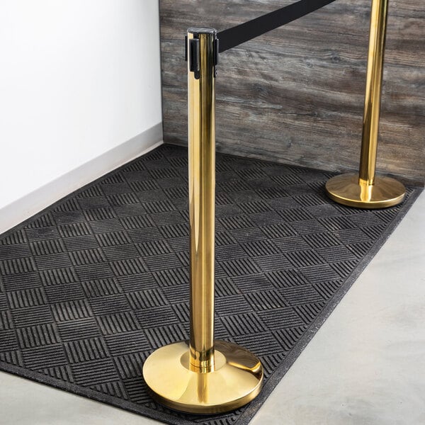 A Lancaster Table & Seating gold crowd control stanchion with a black and gold retractable belt.