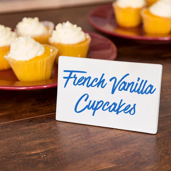 A plate of french vanilla cupcakes with a rectangular ceramic card sign on the table.