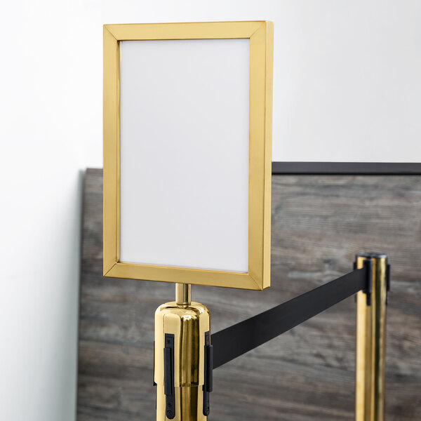 A gold Lancaster Table & Seating vertical sign frame on a black stanchion pole.