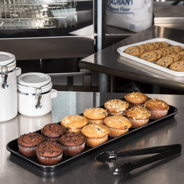 A black Carlisle market tray holding muffins on a counter.