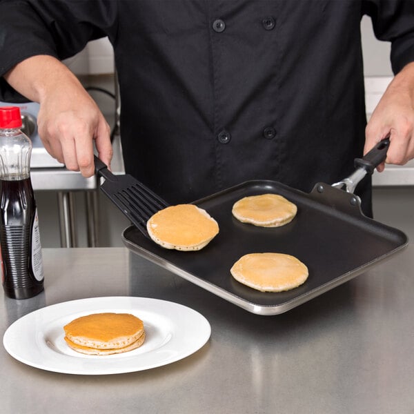 A person in a chef's uniform cooking pancakes on a Vollrath stainless steel non-stick griddle.