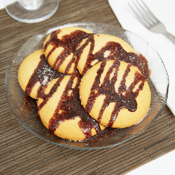 An Arcoroc glass dessert plate with cookies drizzled with chocolate sauce.