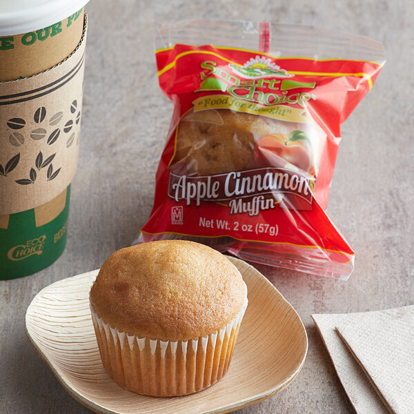 An individually wrapped apple cinnamon muffin on a plate with a cup of coffee.
