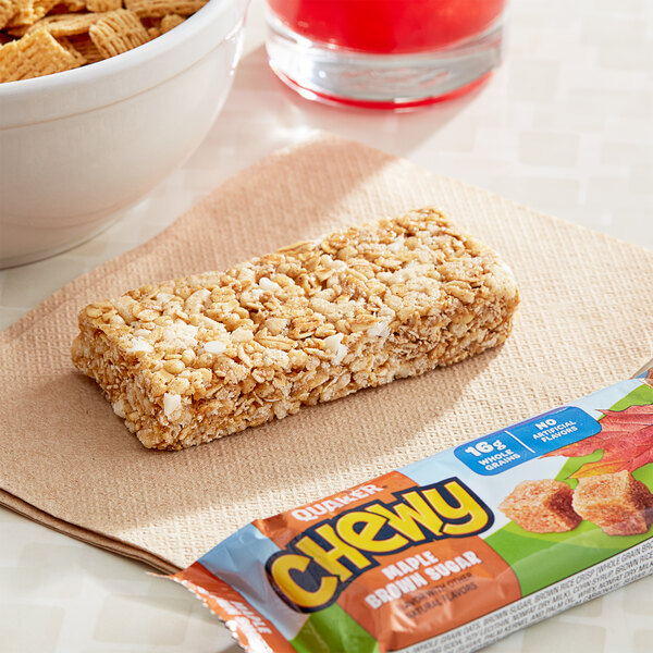 A Quaker Chewy Maple Brown Sugar Granola Bar on a napkin next to a bowl of cereal.