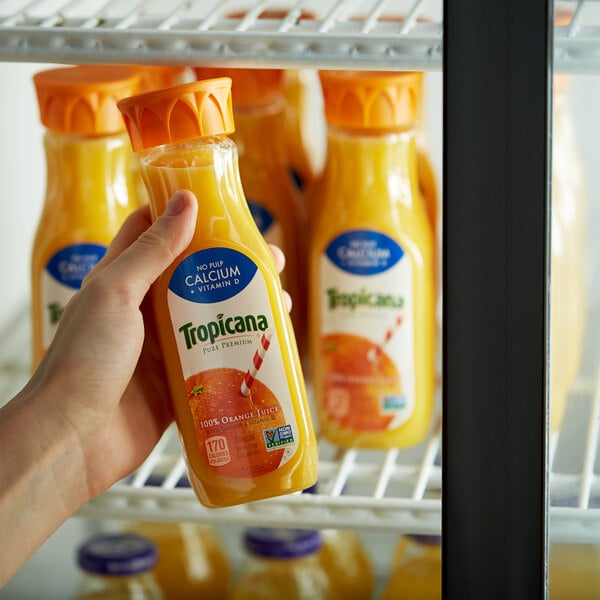A close-up of a hand holding a bottle of Tropicana Calcium Added No Pulp Pure Premium Orange Juice.