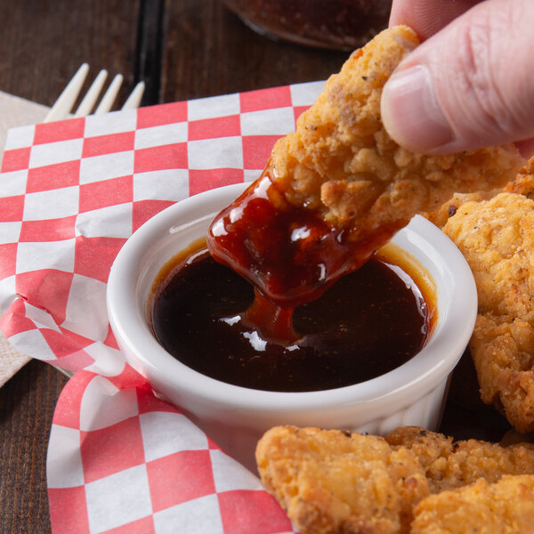 A person dipping a fried chicken strip into a bowl of Sweet Baby Ray's Citrus Chipotle BBQ sauce.