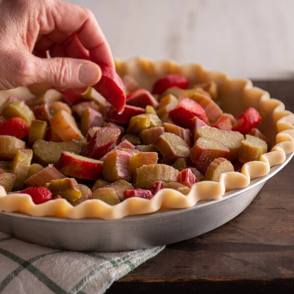 A hand putting a piece of red and green rhubarb into a pie.