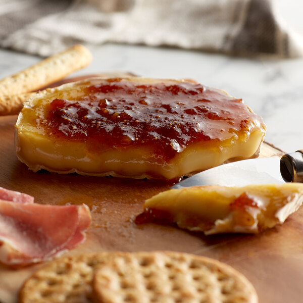 A wooden board with Notre Dame Baby Brie, jam, crackers, and bread.