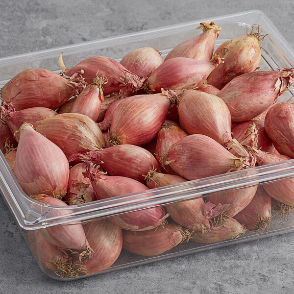 A plastic container of unpeeled shallots on a counter.