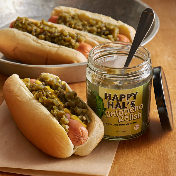 A hot dog with Cortazzo jalapeno relish and mustard next to a jar of Cortazzo jalapeno relish.