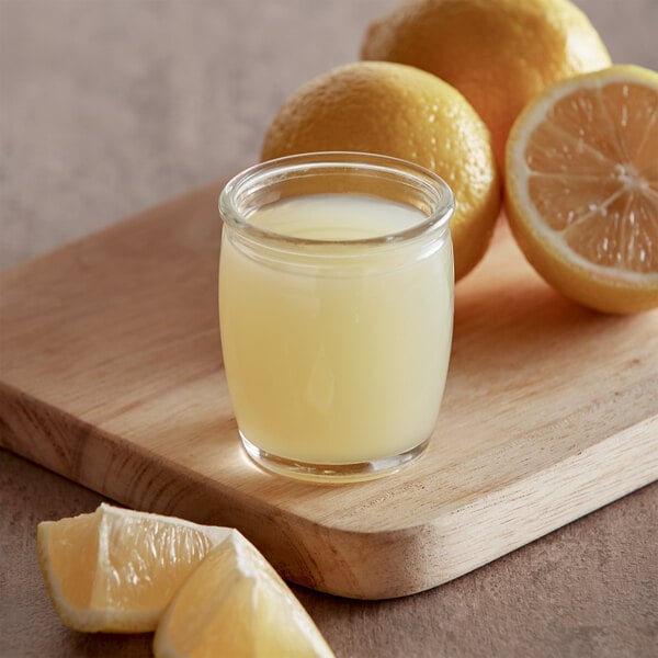 A glass of Sunkist lemon juice next to lemons on a counter.
