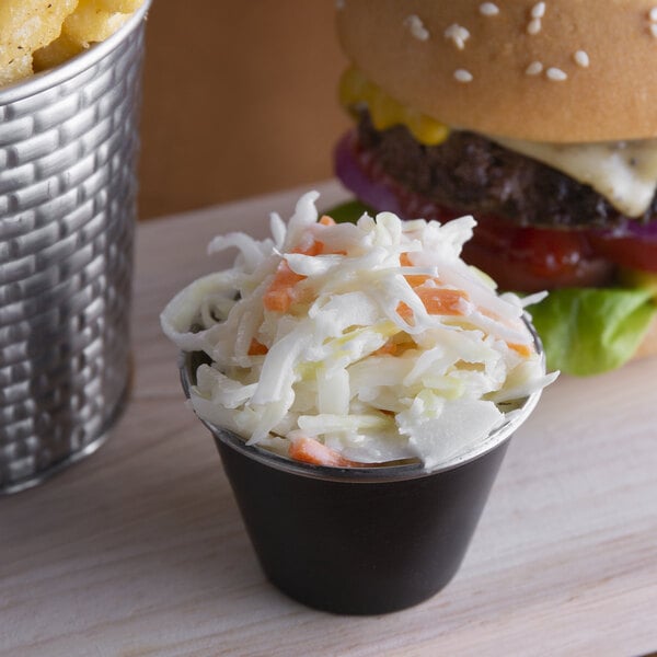 A cup of Spring Glen Fresh Foods shredded coleslaw on a table next to a burger.