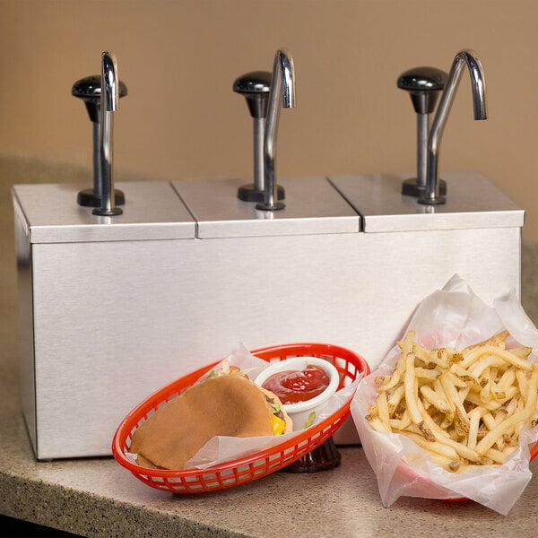 A Carlisle stainless steel pump condiment dispenser with a basket of fries and a burger on a counter.