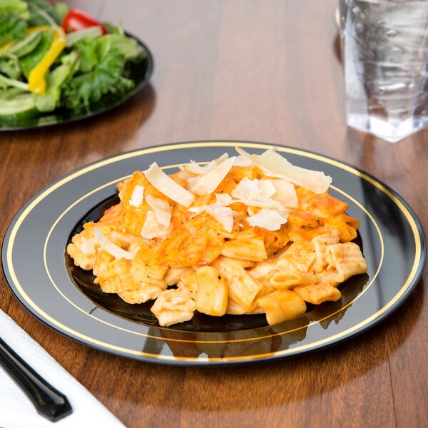 A Fineline Black plastic plate with gold bands holding pasta, chicken, and vegetables.