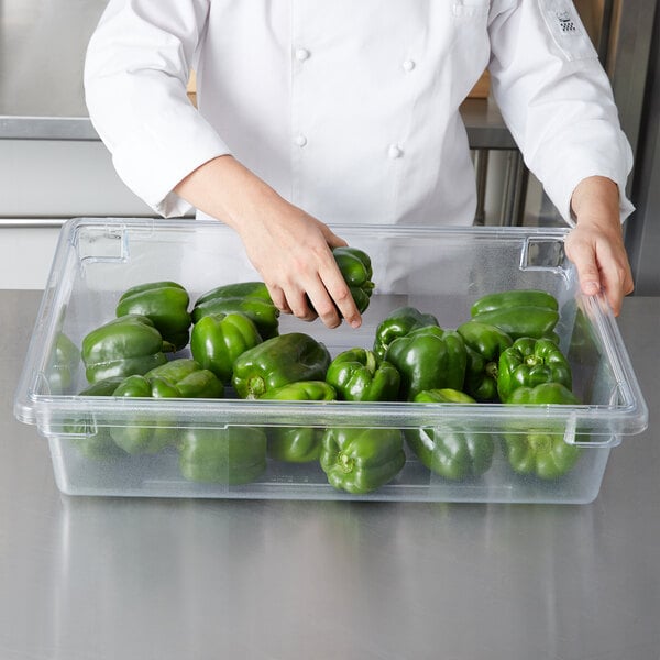 A chef putting green bell peppers in a Rubbermaid clear polycarbonate food storage container.