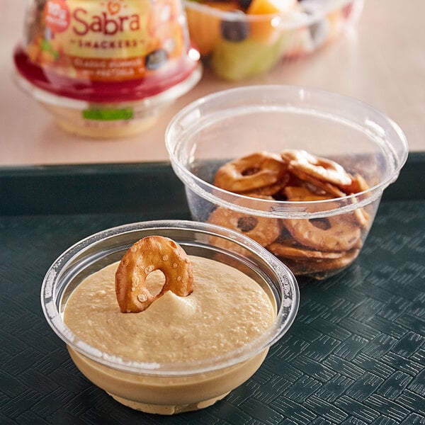 A plastic container with a bowl of Sabra Classic Hummus and Rold Gold pretzels on a tray.
