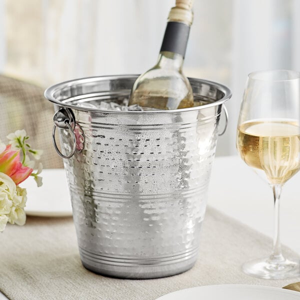 A bottle of wine in a silver bucket of ice on a table.