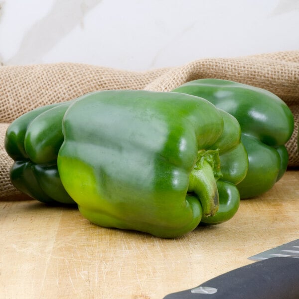 A close-up of three large green bell peppers on a cutting board.