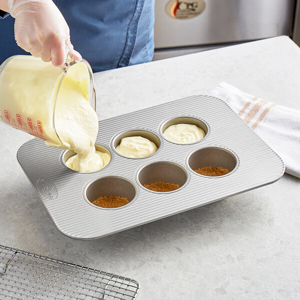 A person pouring batter into a Chicago Metallic mini cheesecake pan.