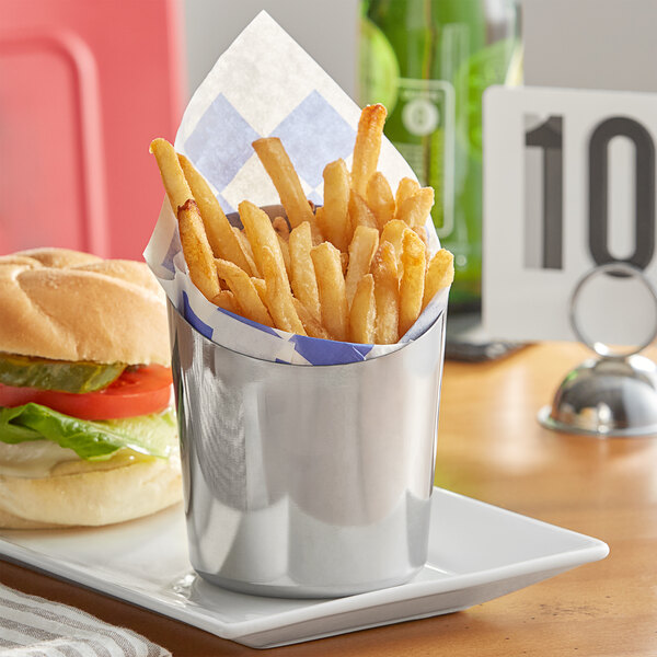 A silver Acopa stainless steel container full of french fries sits on a table with a plate of french fries and a burger.