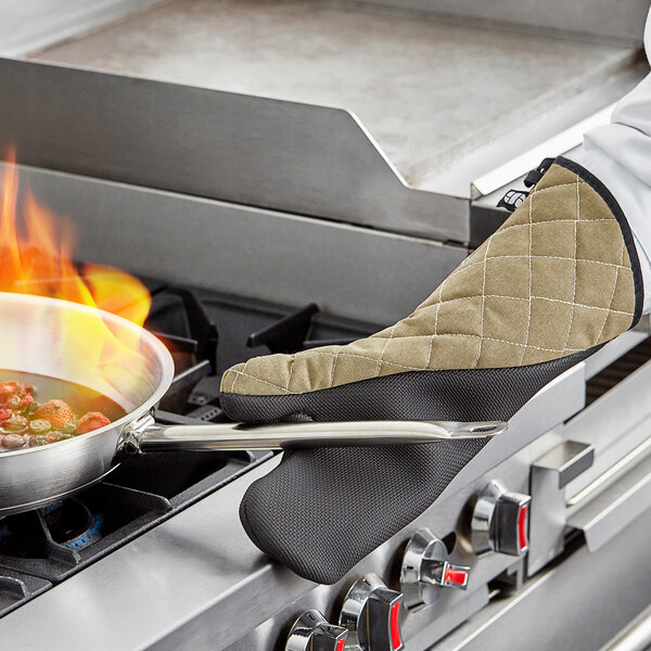 A person wearing a San Jamar oven mitt cooking food on a stove.