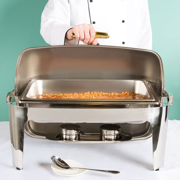 A person using an American Metalcraft Adagio stainless steel chafing dish on a table outdoors.