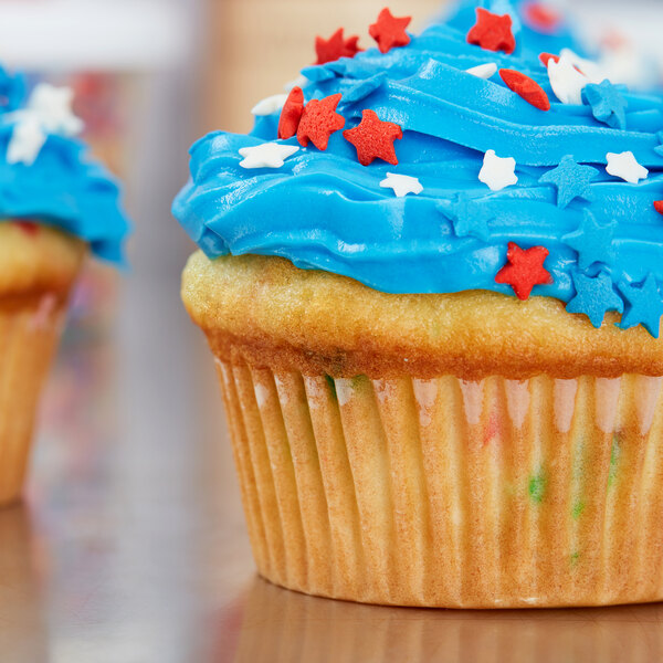 A white Hoffmaster fluted baking cup with a cupcake with blue frosting and red and white stars.