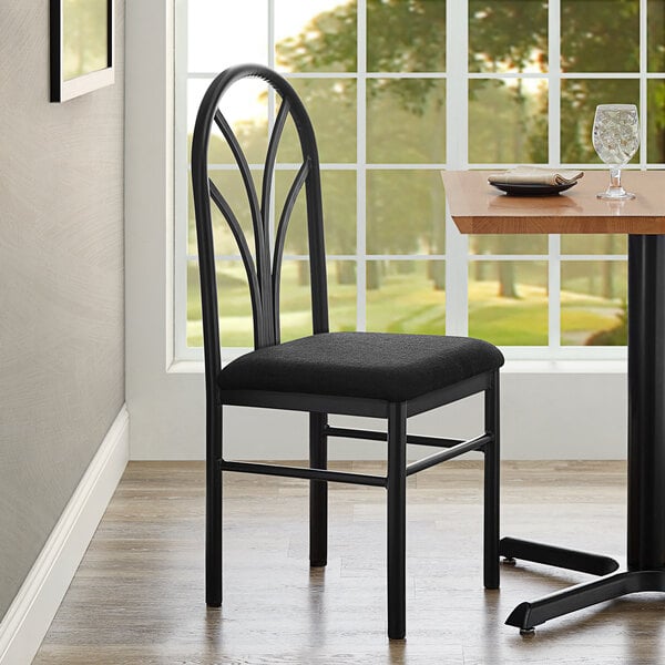 A Lancaster Table & Seating Spoke Back chair with a detached black fabric seat on a wood floor next to a table.