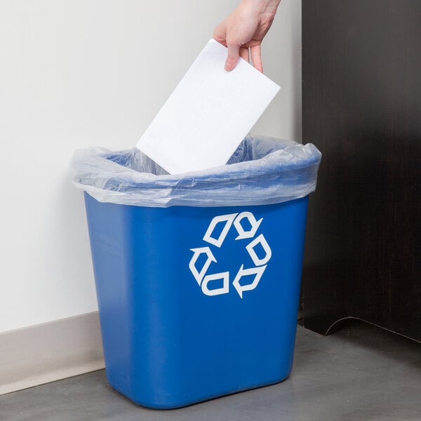 A hand putting a paper into a blue Rubbermaid recycling bin.