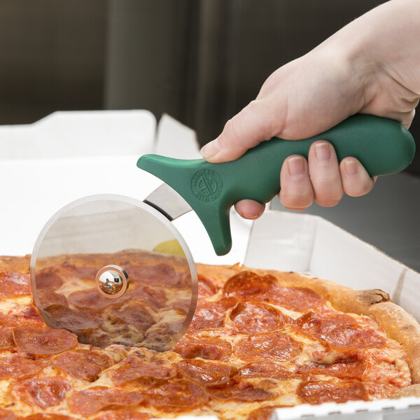 A hand with a green handle using an American Metalcraft pizza cutter to cut a pizza.