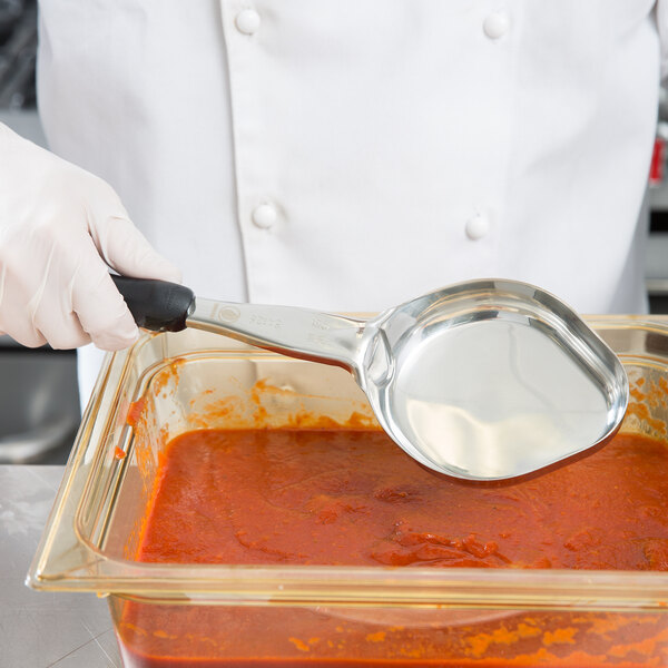 A hand in white gloves using a Vollrath black solid oval Spoodle to serve red sauce.