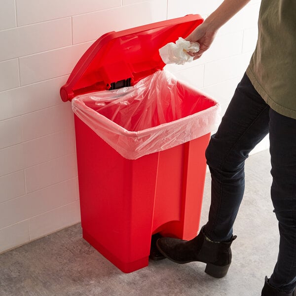 A person putting a plastic bag in a red Lavex rectangular step-on trash can.