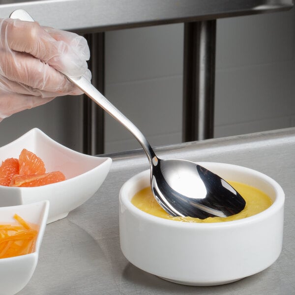 A person in gloves using a Mercer Culinary plating spoon to serve yellow liquid.