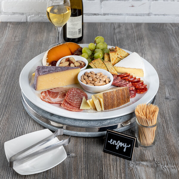 A round soapstone platter with a plate of food, a glass of wine, and a slice of cheese on a table.