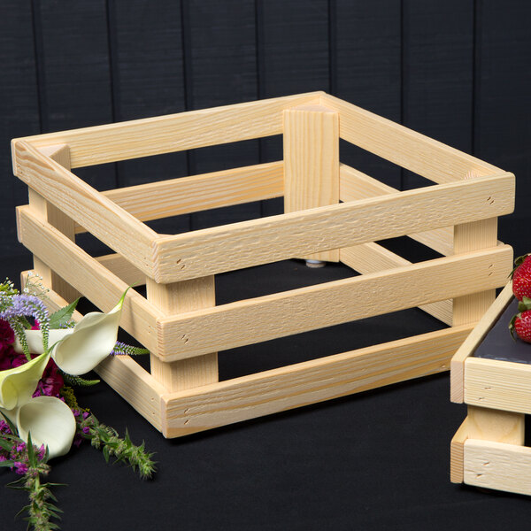 A wooden crate with strawberries and flowers on a table with a black surface.