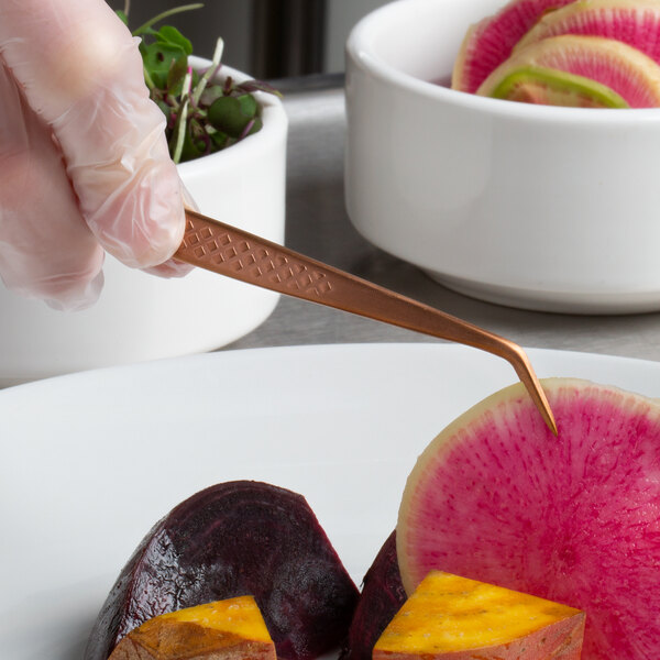Mercer Culinary rose gold fine point curved tip plating tongs being used to plate vegetables.