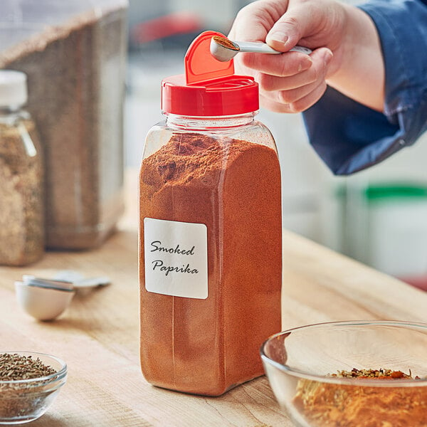 A person pouring a spice into a rectangular plastic spice container.