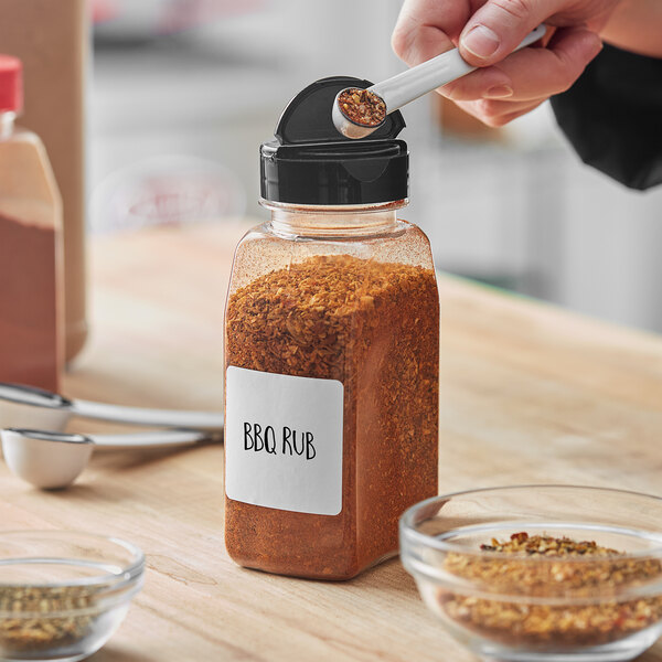 A person putting seasoning in a rectangular plastic spice jar.