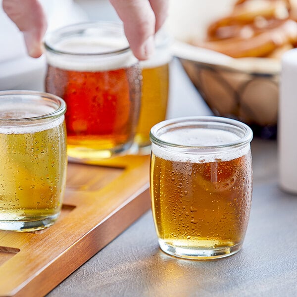 A person holding a tray of Acopa beer tasting glasses filled with beer on a table in a brewery tasting room.