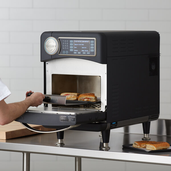 A man cooking food in a TurboChef Sota rapid cook oven on a countertop.