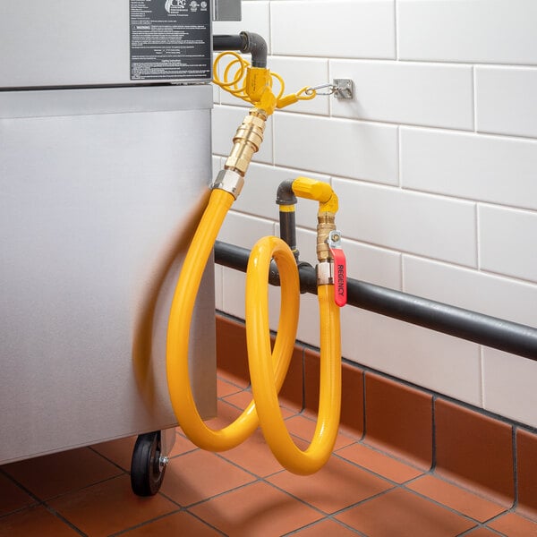 A yellow Regency gas connector hose kit with swivel connectors and elbows attached to a metal container.