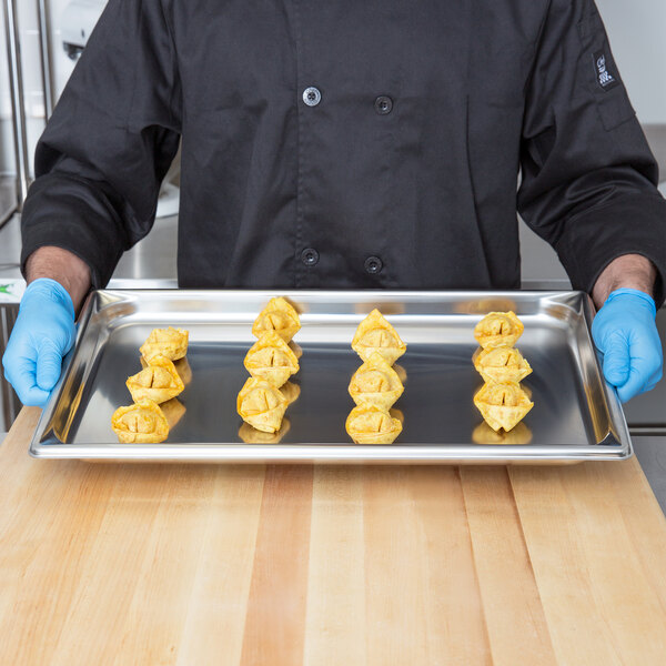 A man in a chef's uniform holding a Vollrath stainless steel steam table tray of wontons.