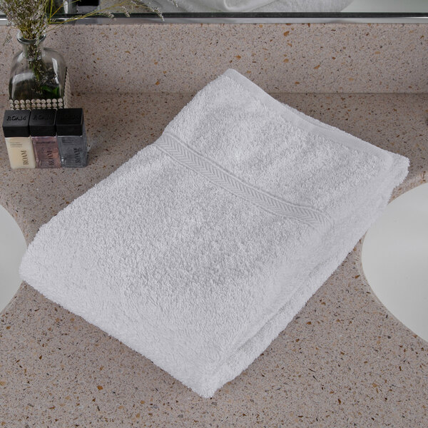 An Oxford Gold white cotton polyester blend bath towel with a cam border on a counter top.