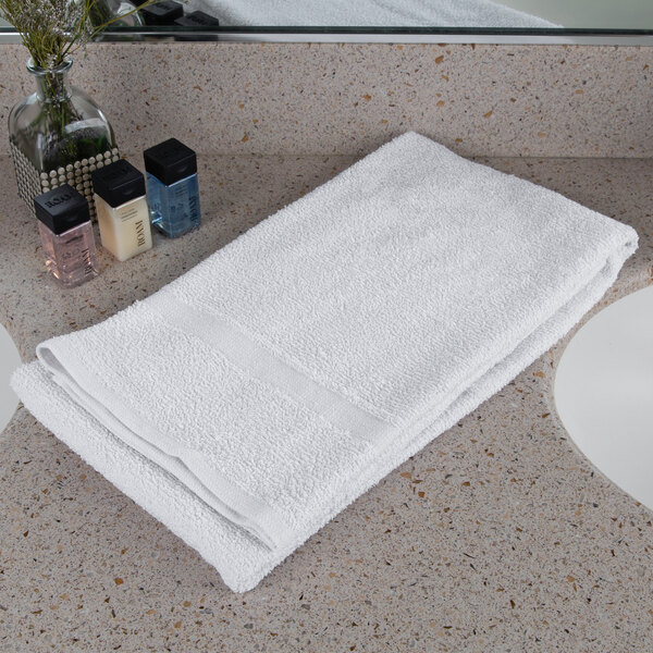 An Oxford Gold white cotton polyester blend bath towel with a cam border on a white counter.