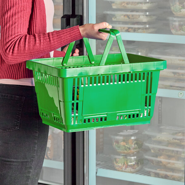 A green plastic grocery market shopping basket with plastic handles being carried by a person.