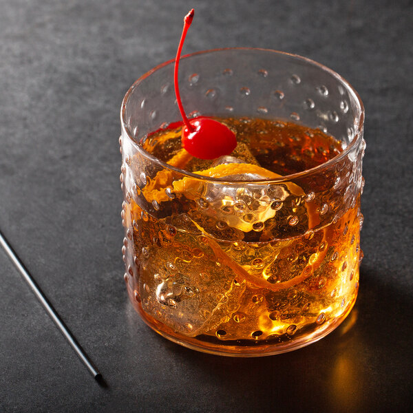 A Acopa Hobnail rocks glass with a brown drink, ice, and a cherry on top.