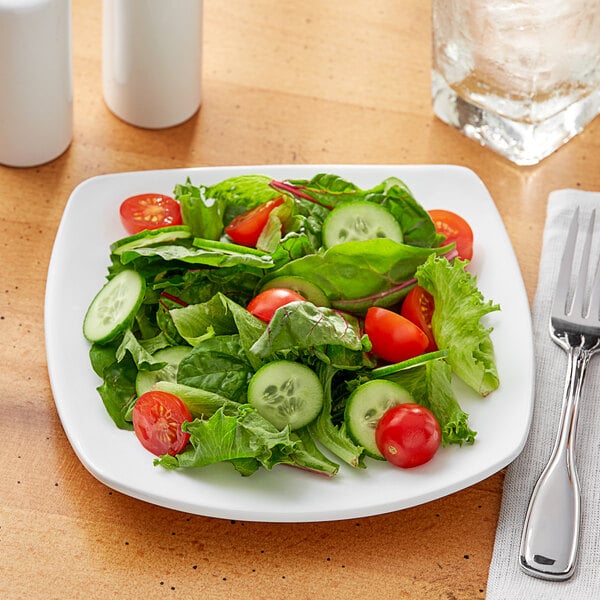 A plate of salad with tomatoes, cucumbers, and lettuce on a white Acopa square porcelain plate.