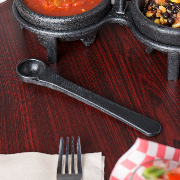 A close-up of a black HS Inc. polyethylene condiment spoon in a bowl of salsa on a table.